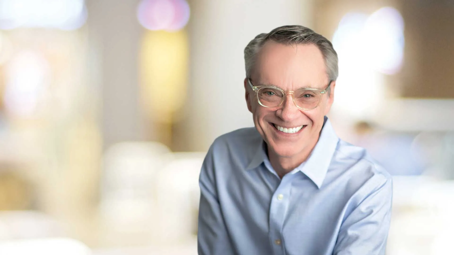 Smiling middle-aged man with glasses wearing a light blue shirt against a soft blurred background