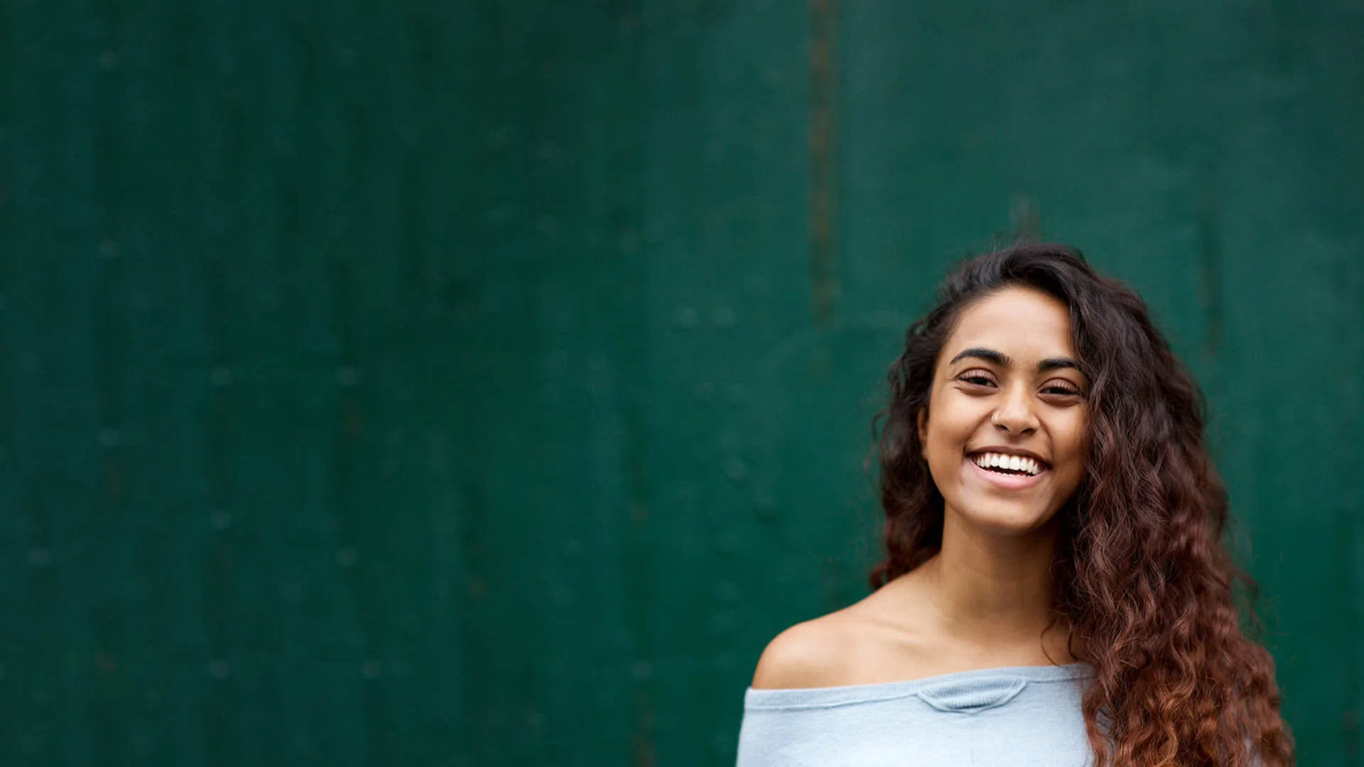 Smiling young woman with long curly hair wearing off-shoulder top against green textured background