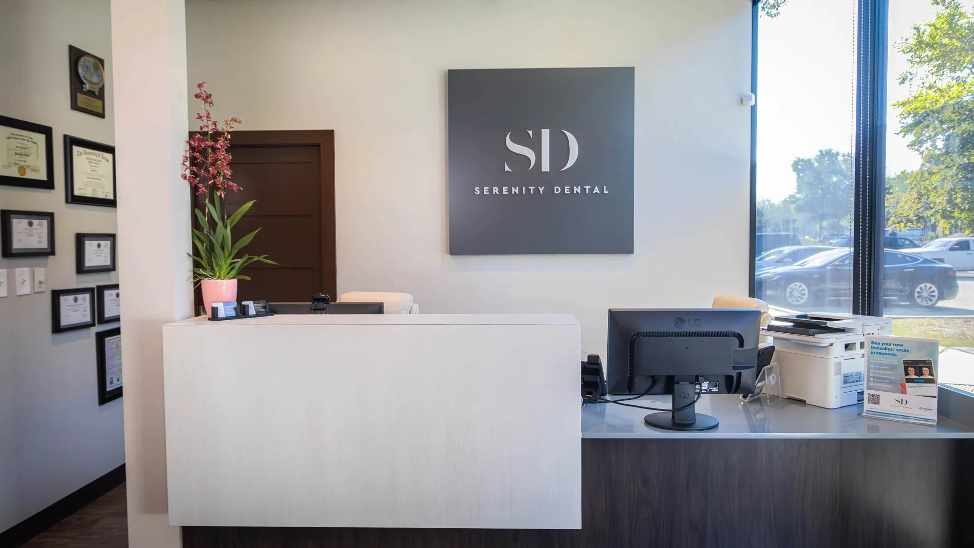 Modern dental office reception with Serenity Dental sign, computer, certificates, and large window with natural light.
