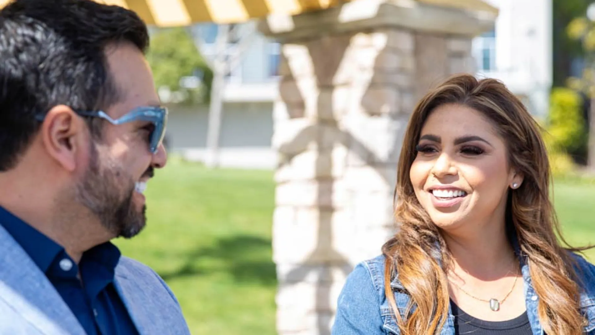 Two smiling individuals enjoying a sunny day outdoors while seated on a bench.