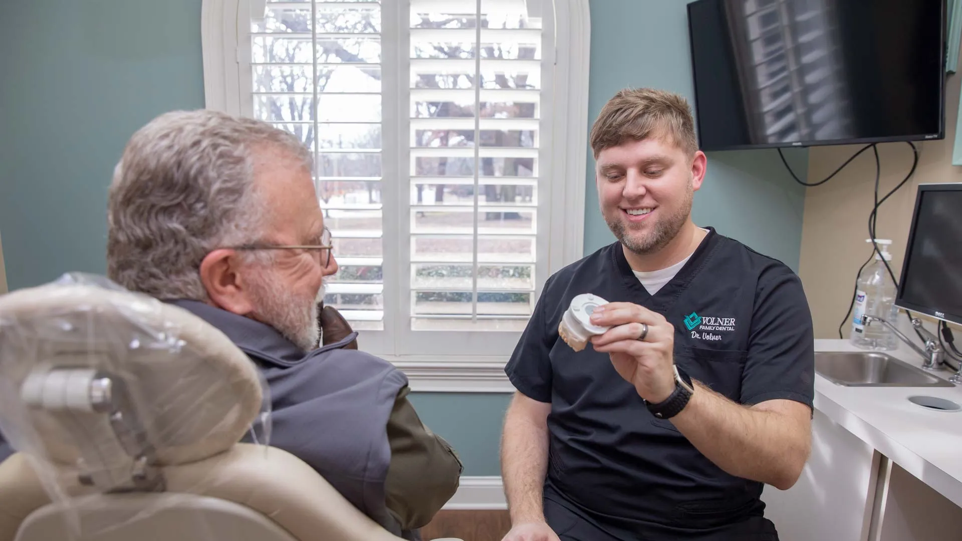 Dentist explaining dental mold to a senior male patient in a bright dental office.