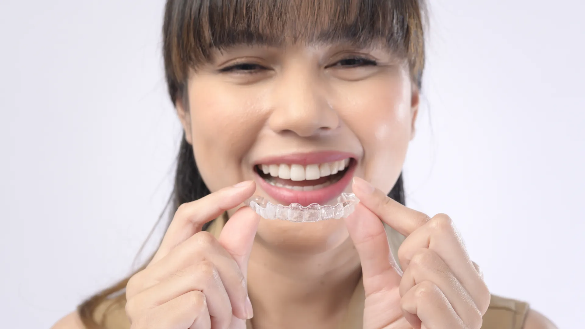 Smiling woman holding a clear dental aligner for teeth straightening close to her mouth.