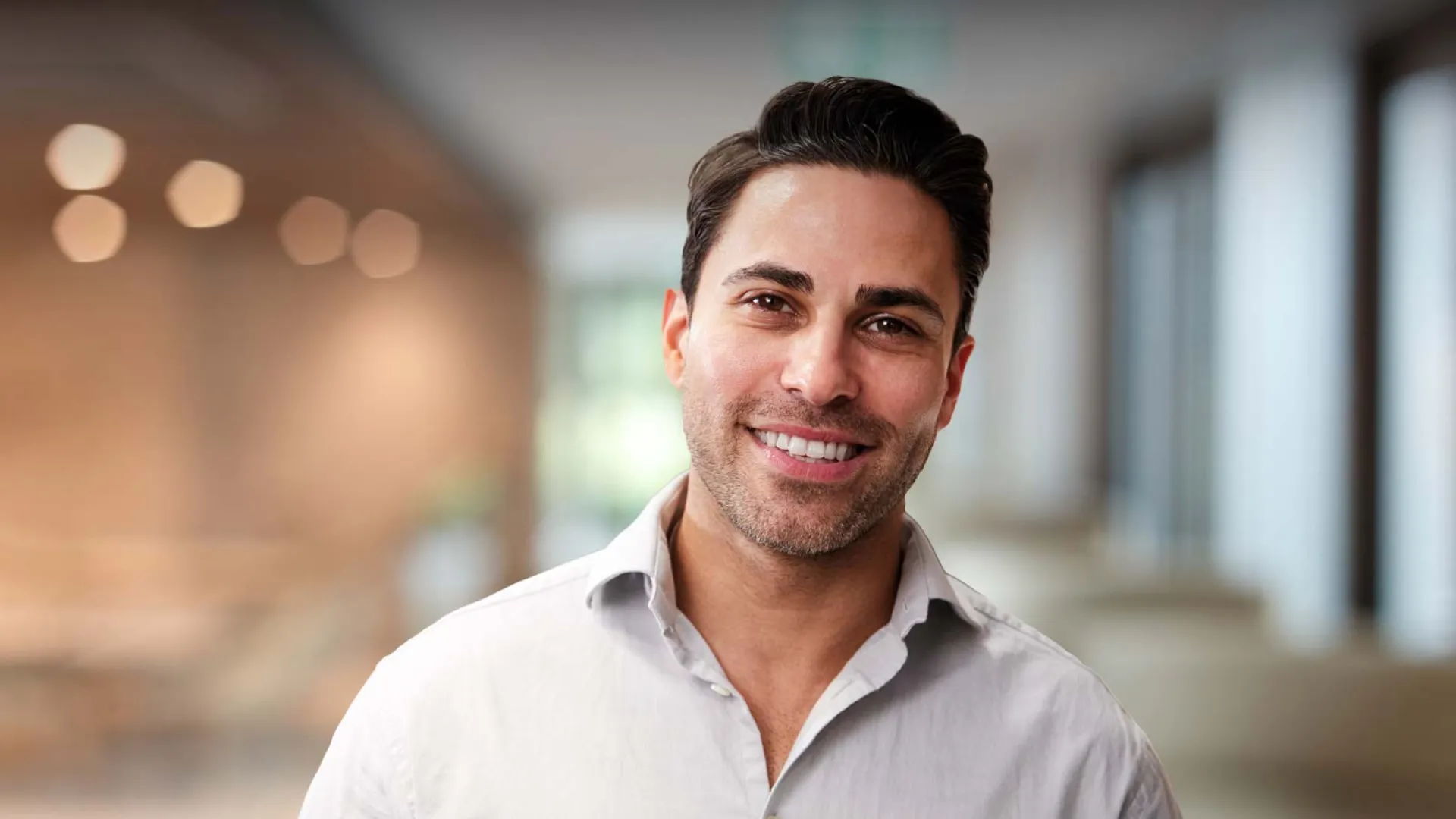 Smiling man in a casual shirt, bright office background with bokeh effect.