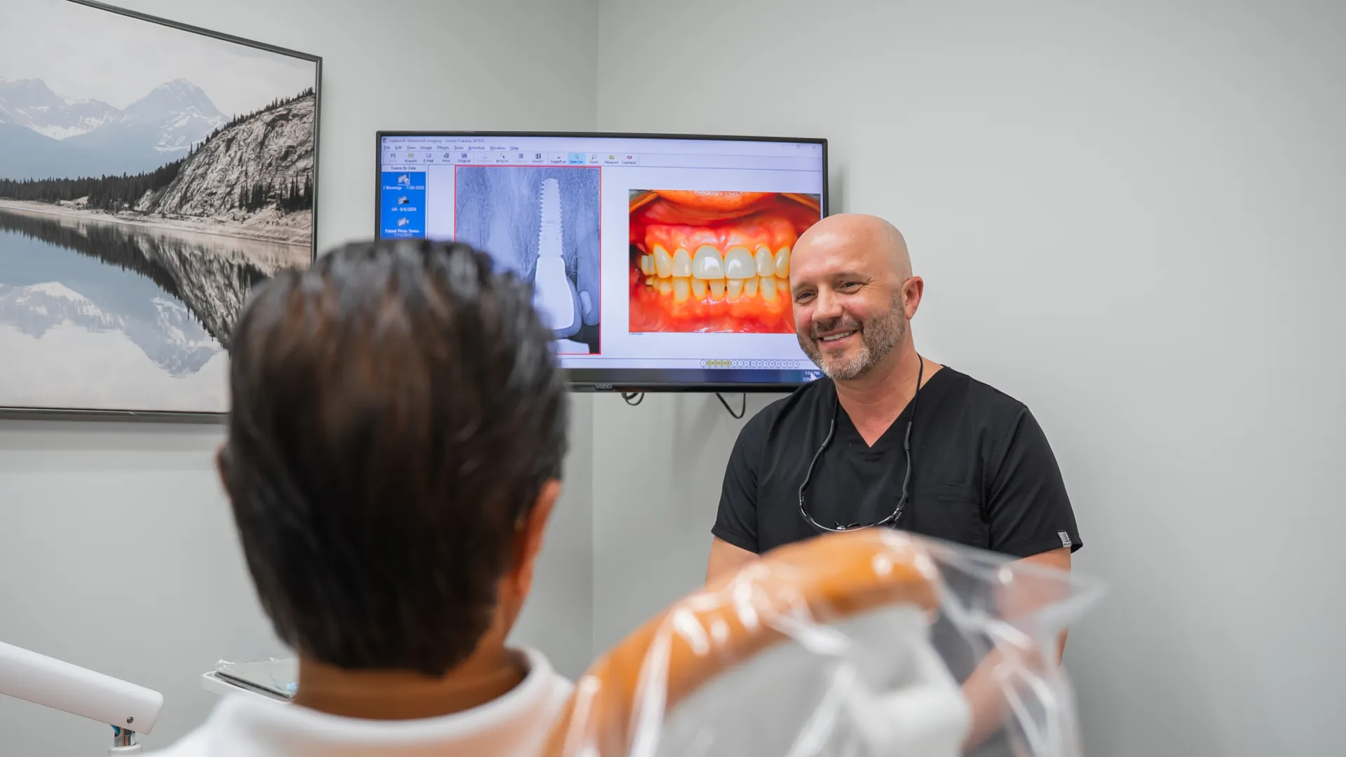 Dentist explaining dental implant and teeth X-ray to patient in modern clinic with screen display.
