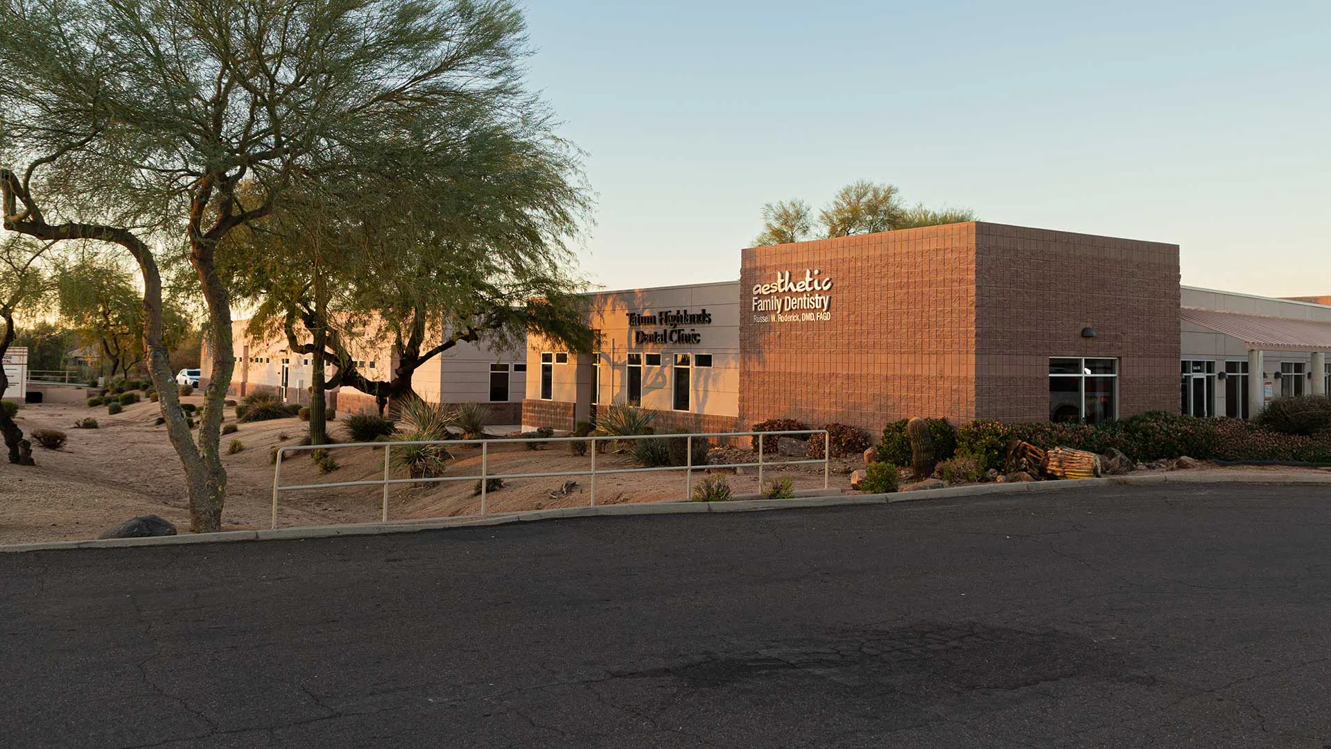 Exterior view of a modern dental clinic surrounded by desert landscaping and trees under a clear sky.