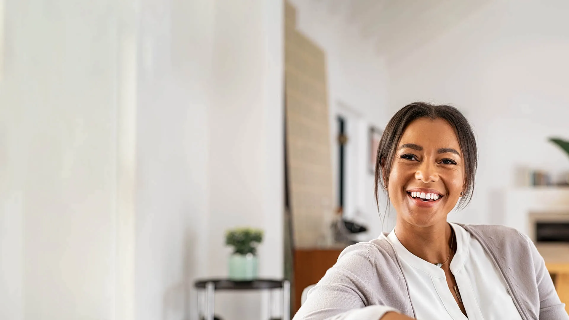Smiling woman indoors, showcasing a warm, welcoming atmosphere with modern decor.