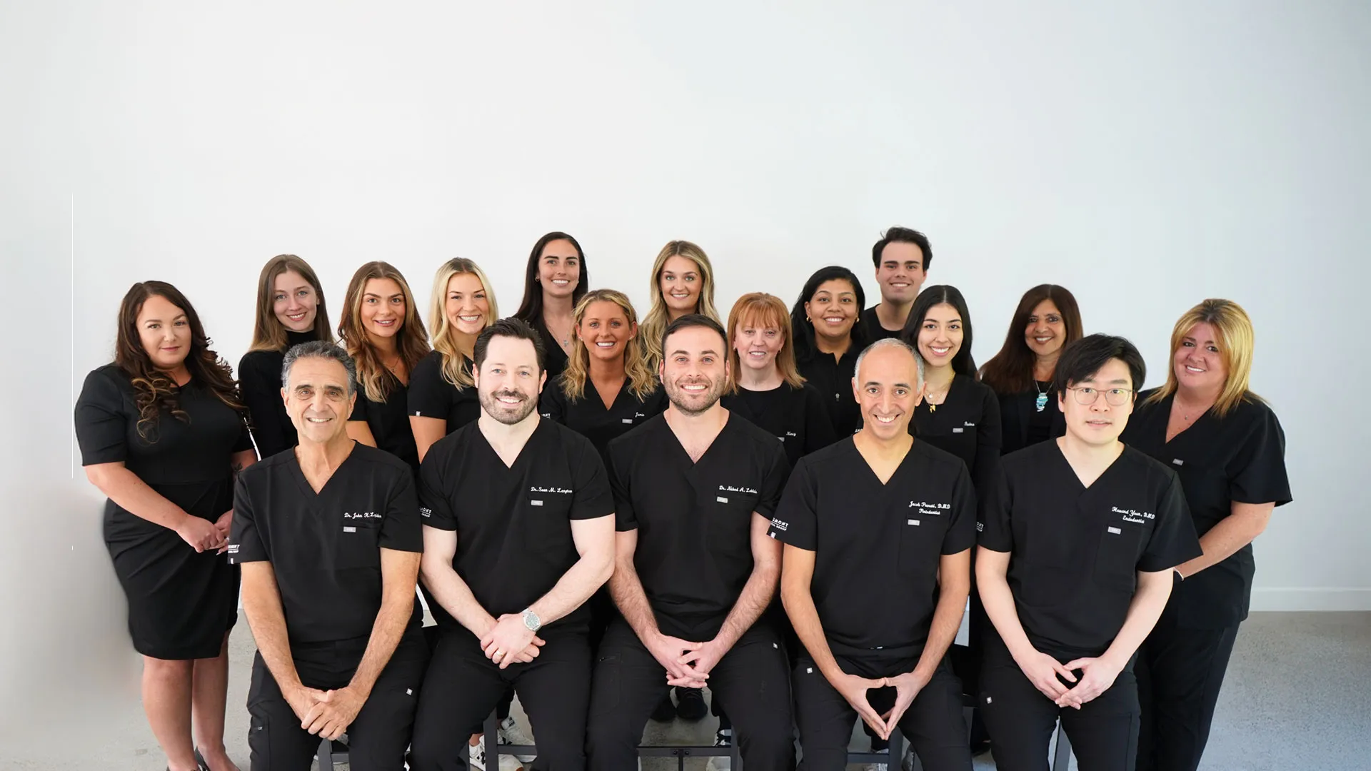 Group photo of healthcare professionals in black scrubs posing together in a well-lit studio.