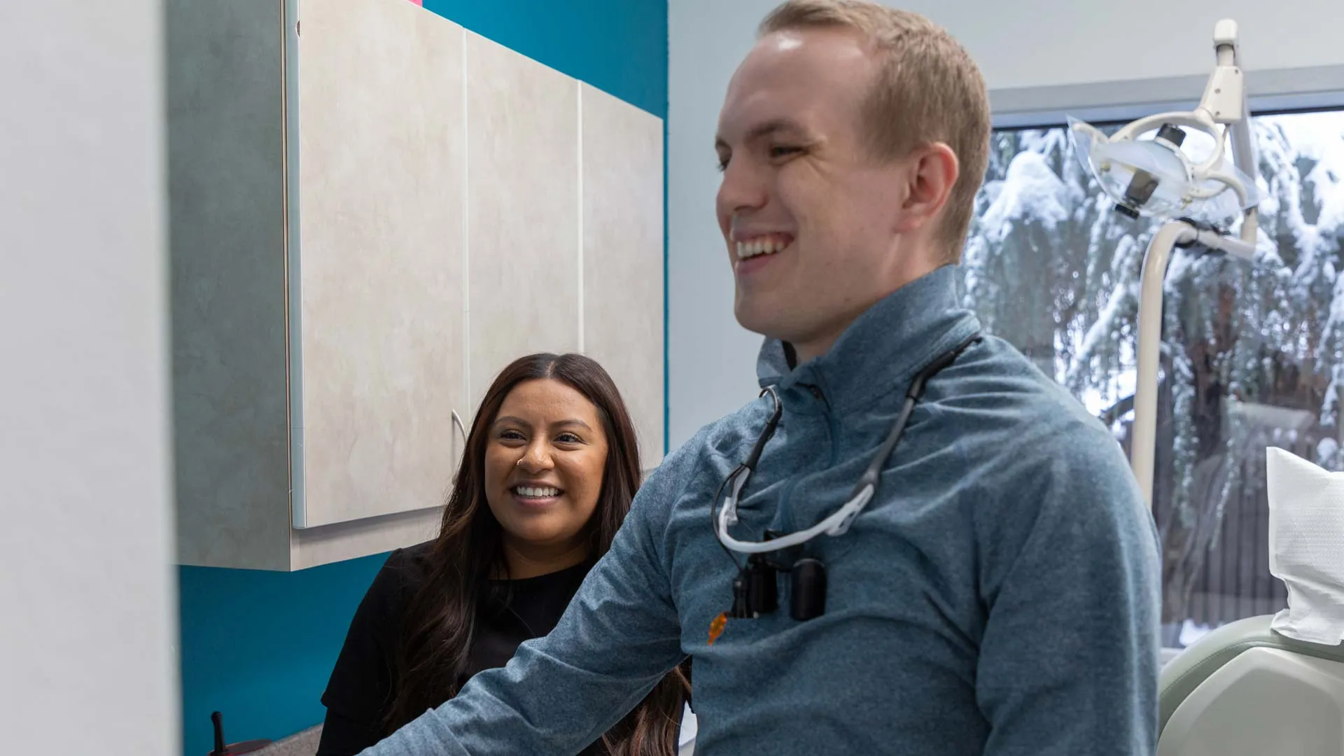 Smiling dentist in blue jacket showing patient something on computer screen in dental office