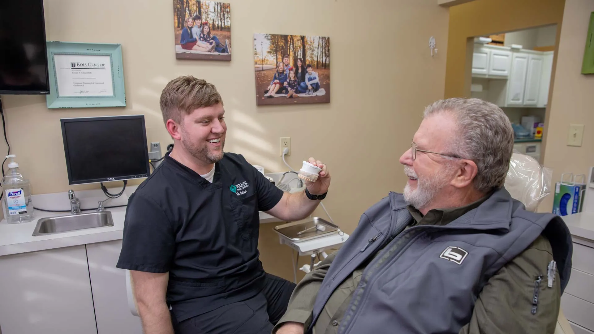 Dentist showing dental mold to a smiling elderly male patient in a bright dental office.