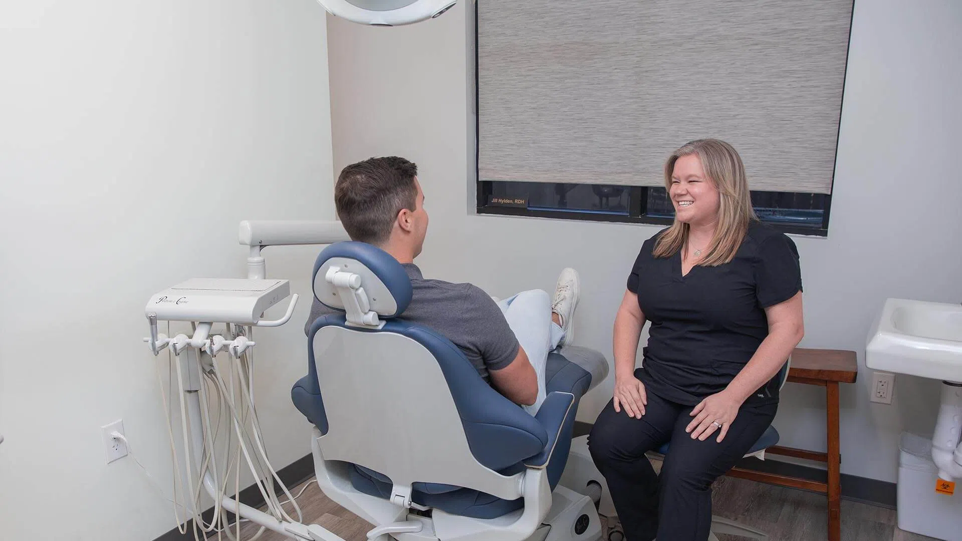 Dentist consults with patient in a modern dental office with equipment and chairs visible