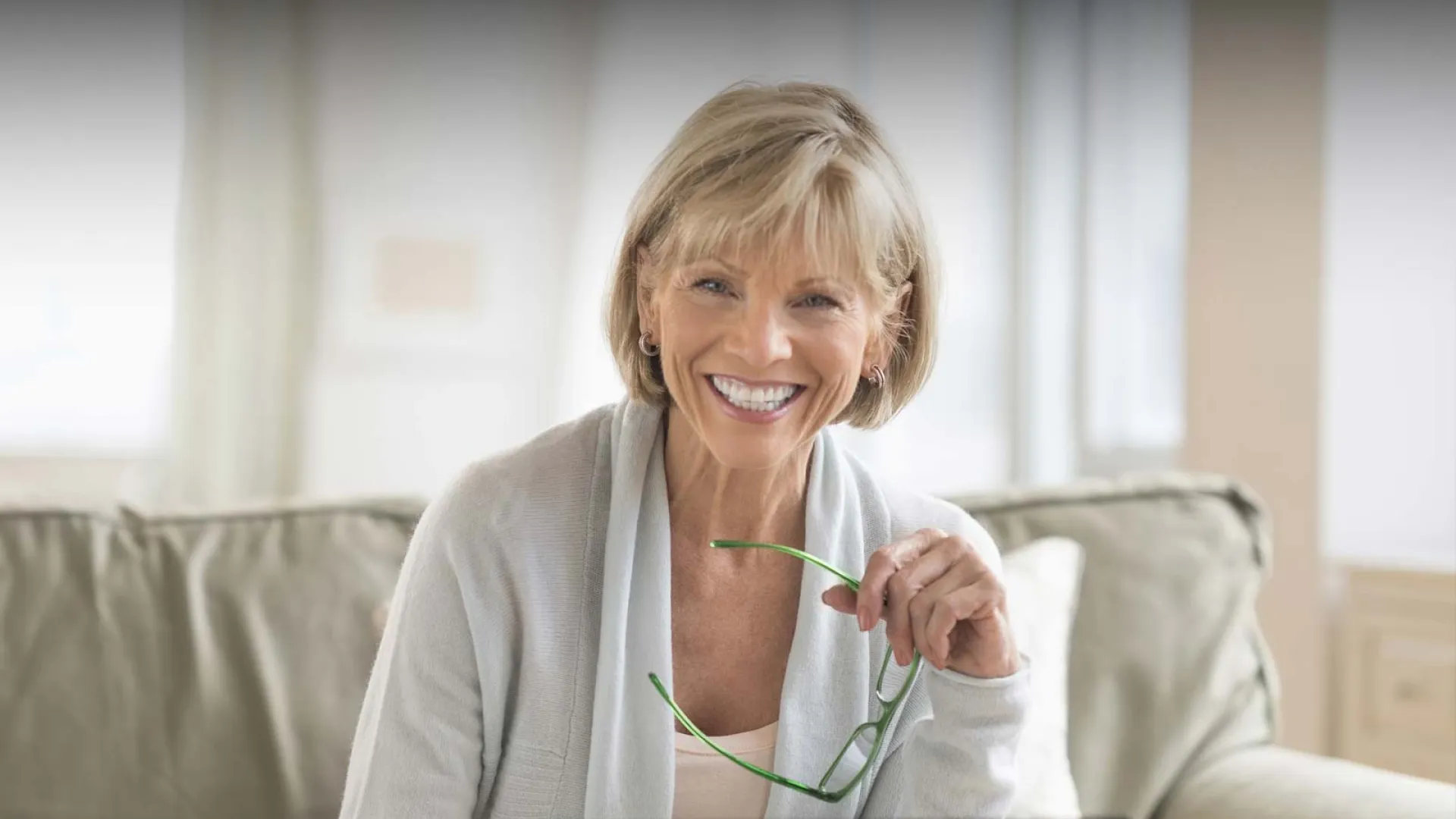 Smiling older woman with glasses sitting on a couch using a laptop, conveying happiness and engagement.