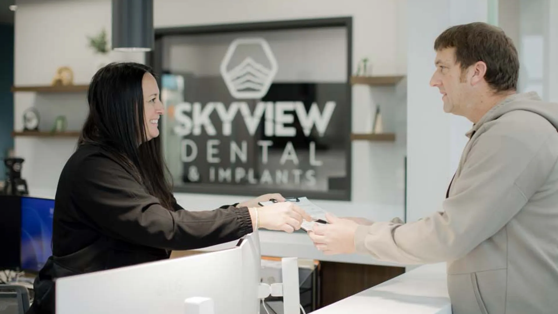 Receptionist handing paperwork to a smiling male patient at Skyview Dental & Implants front desk