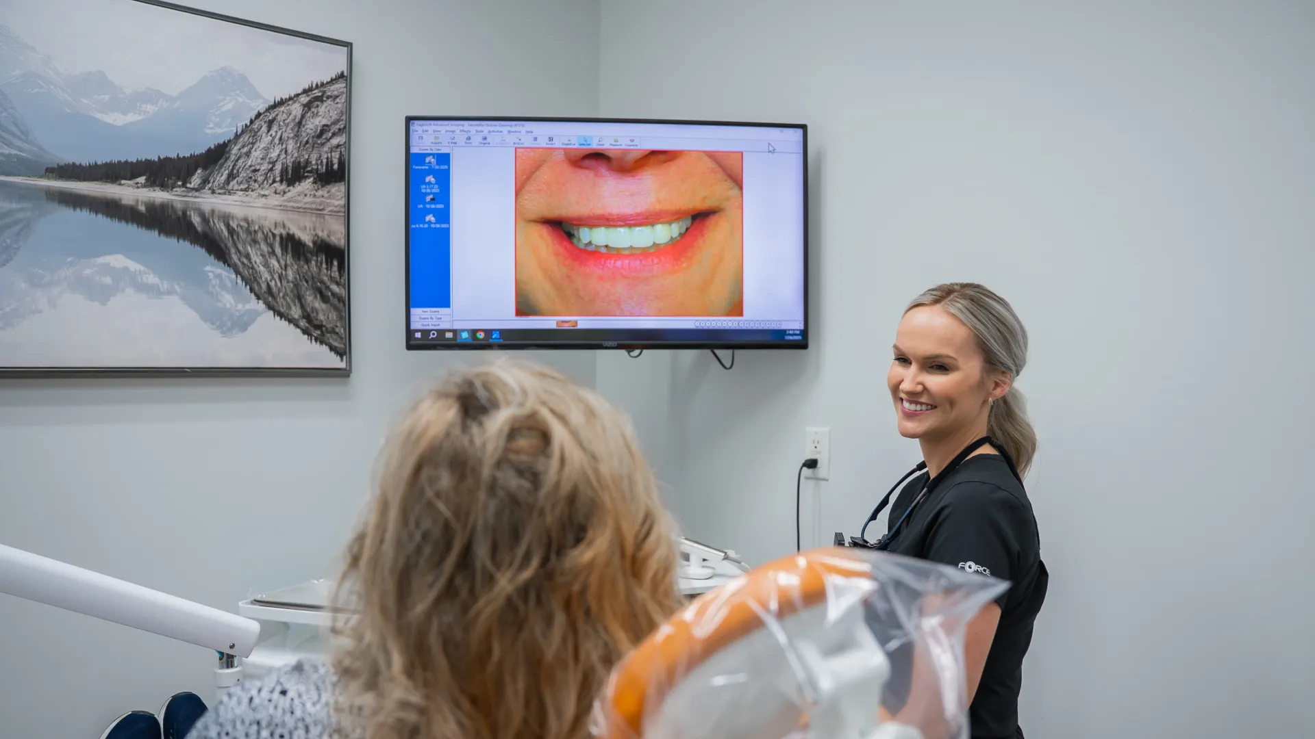 Dental patient viewing smile image on screen with female dentist smiling in clinic room.
