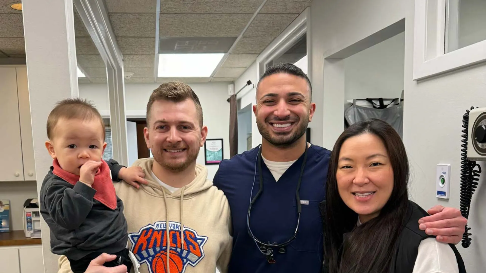 Smiling diverse family and healthcare professional posing together in a medical office hallway.