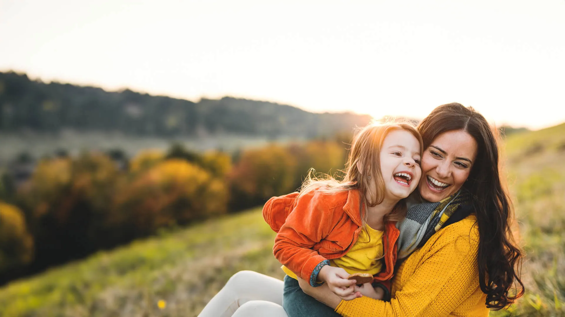 Mother and daughter laughing together outdoors on a sunny autumn day in a grassy field.