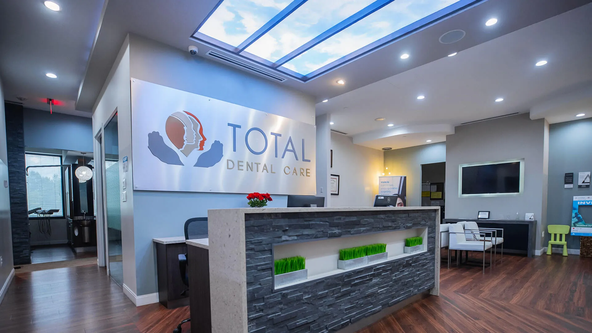 Modern dental office reception area with sleek desk, wood floors, and ceiling light panels simulating a sky.