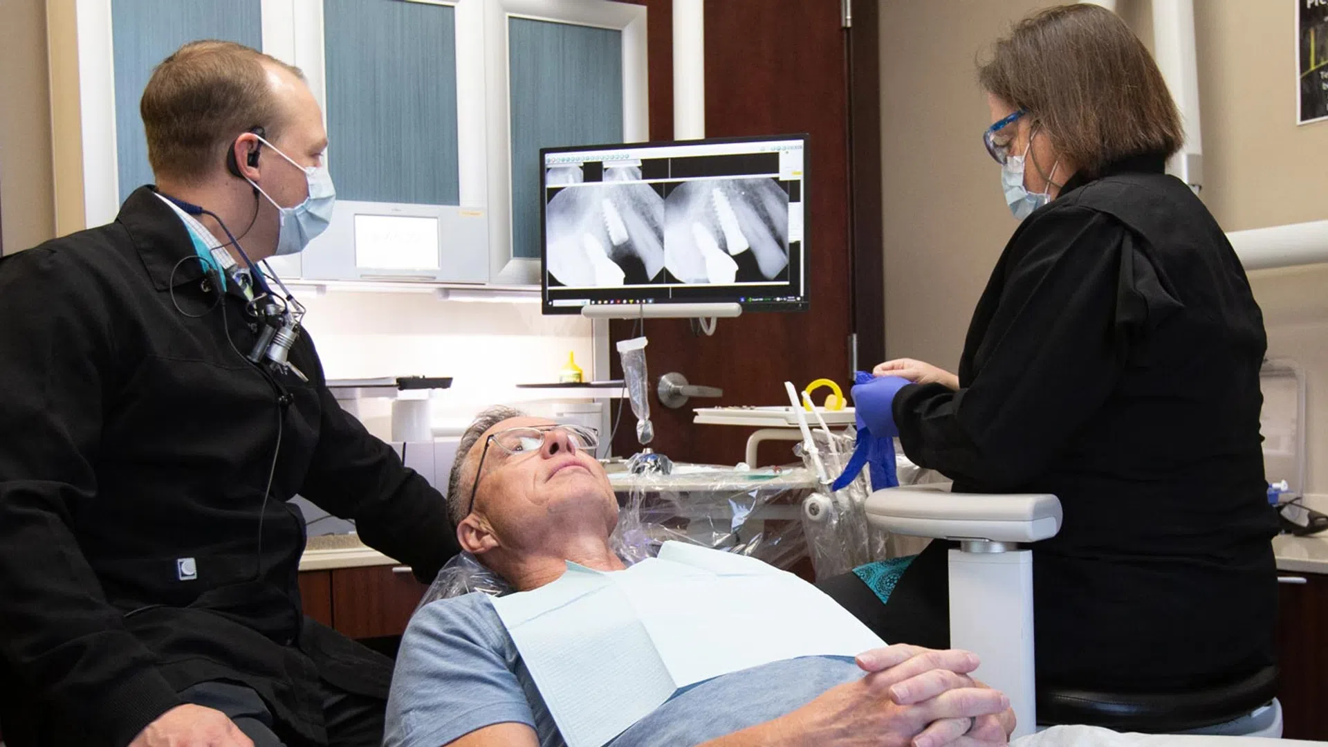 A dental team examines x-rays while a patient relaxes in the chair, promoting dental care and health.