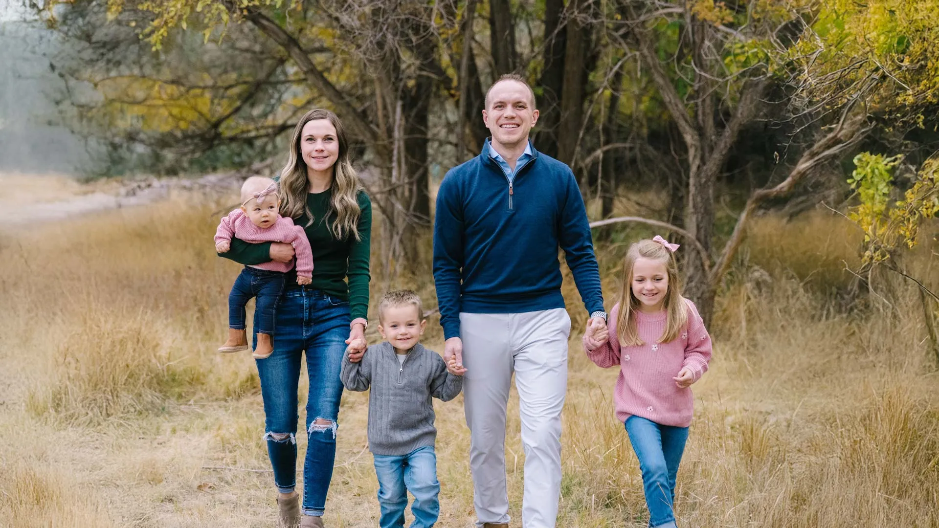 Family of five walking outdoors in autumn with trees and dry grass surrounding them