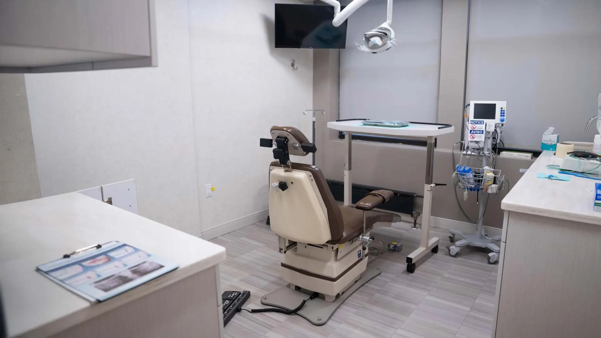 Modern dental clinic room with dentist chair, overhead light, monitor, and dental equipment in a clean setting