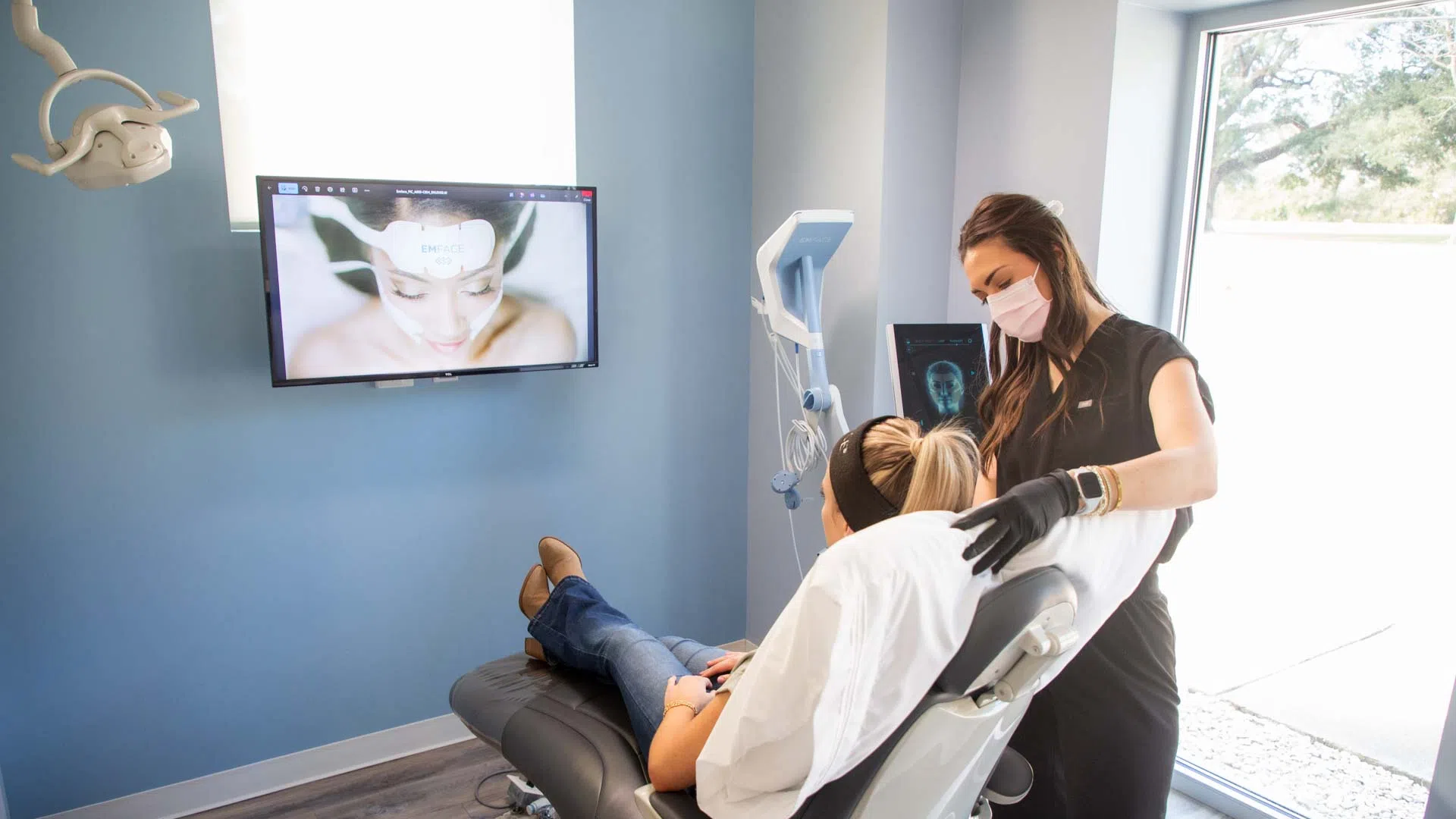 Patient reclines in a modern clinic chair while a masked practitioner provides treatment in a bright room.