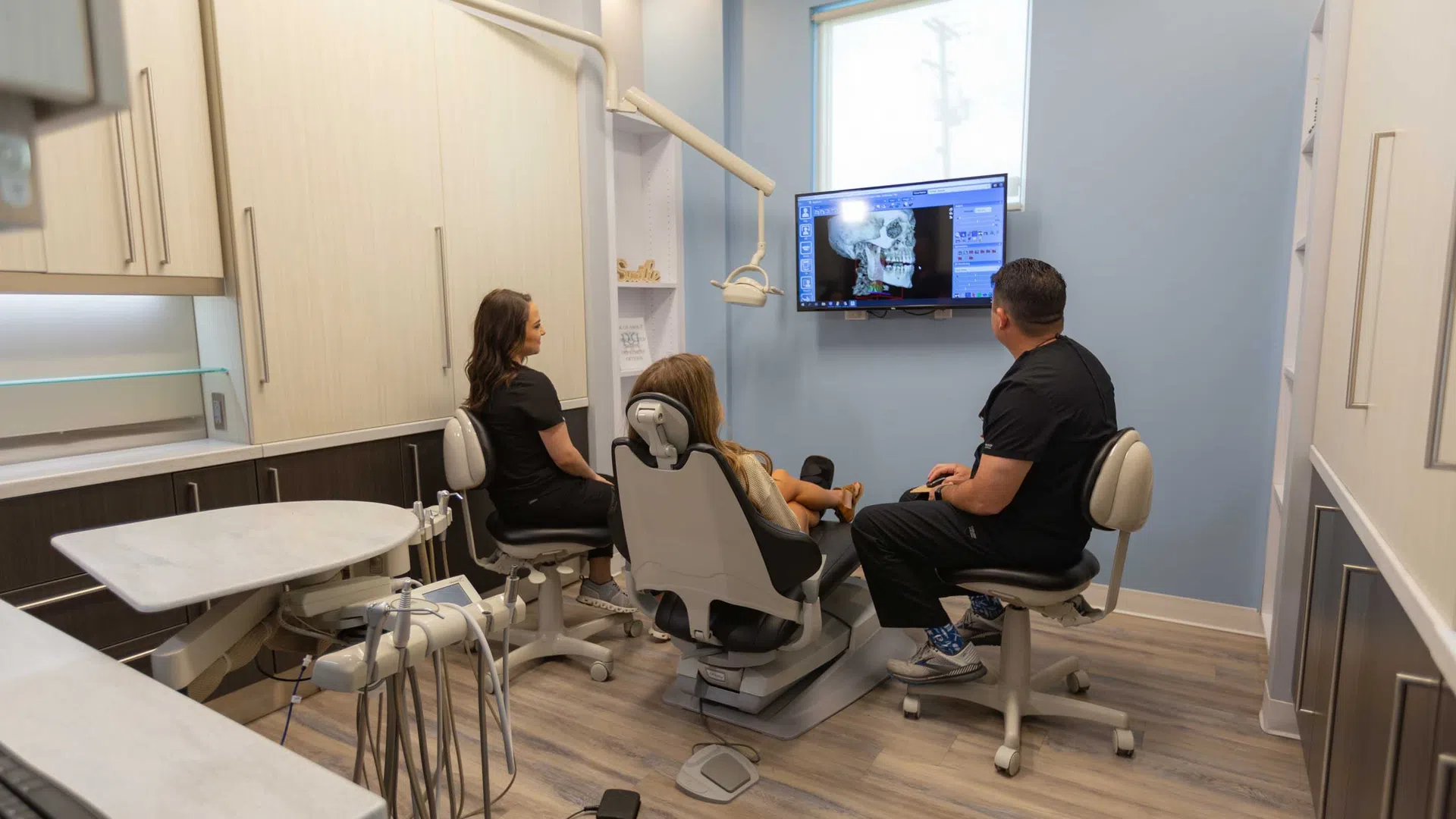 Dentist and assistant reviewing dental X-ray on screen with patient seated in modern dental office chair.