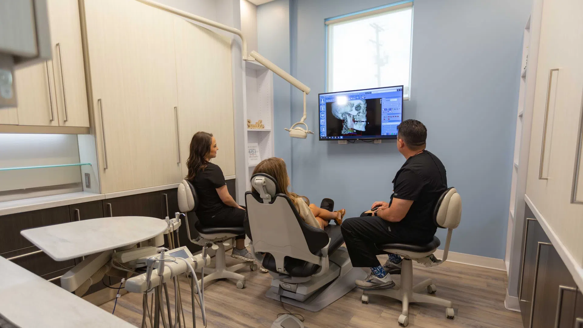 Dentist and assistant reviewing a dental x-ray on a screen with a patient in a modern dental office.