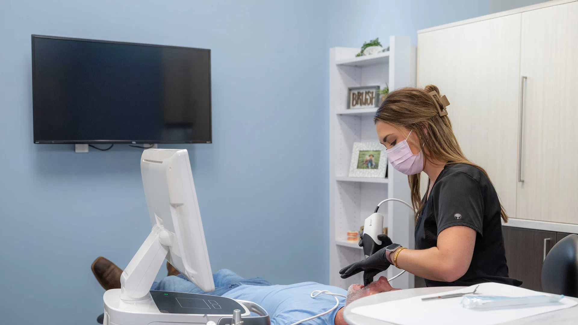Dental professional wearing mask treating patient using advanced dental equipment in modern clinic room.