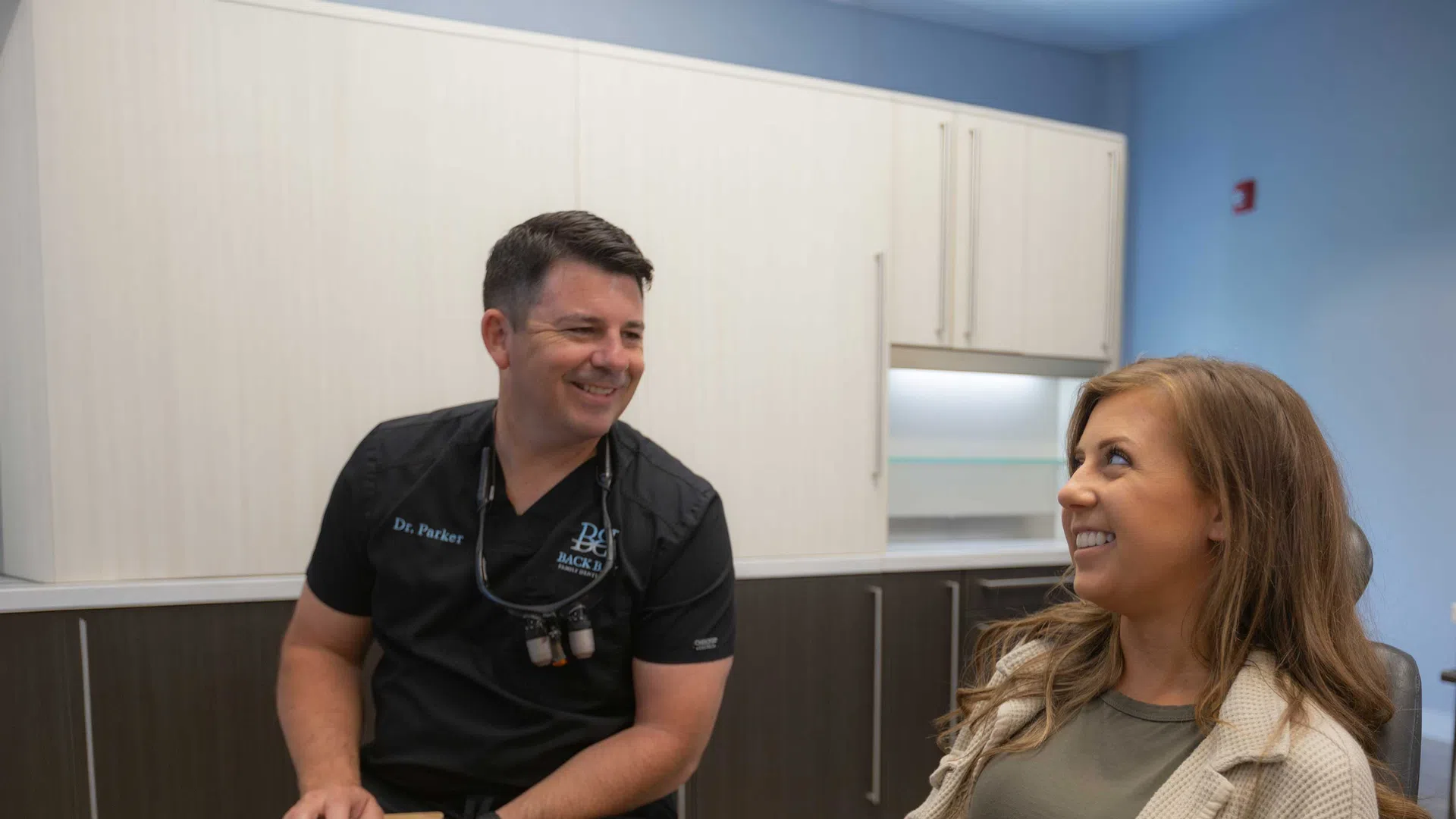 Dentist in black scrubs talking and smiling with female patient in modern dental office