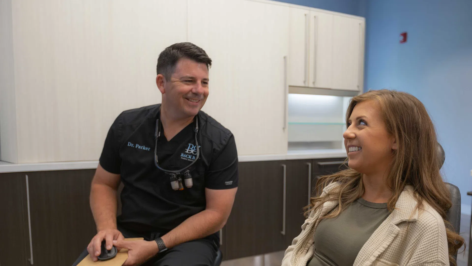 Dentist in black scrubs talking and smiling with female patient in modern dental office