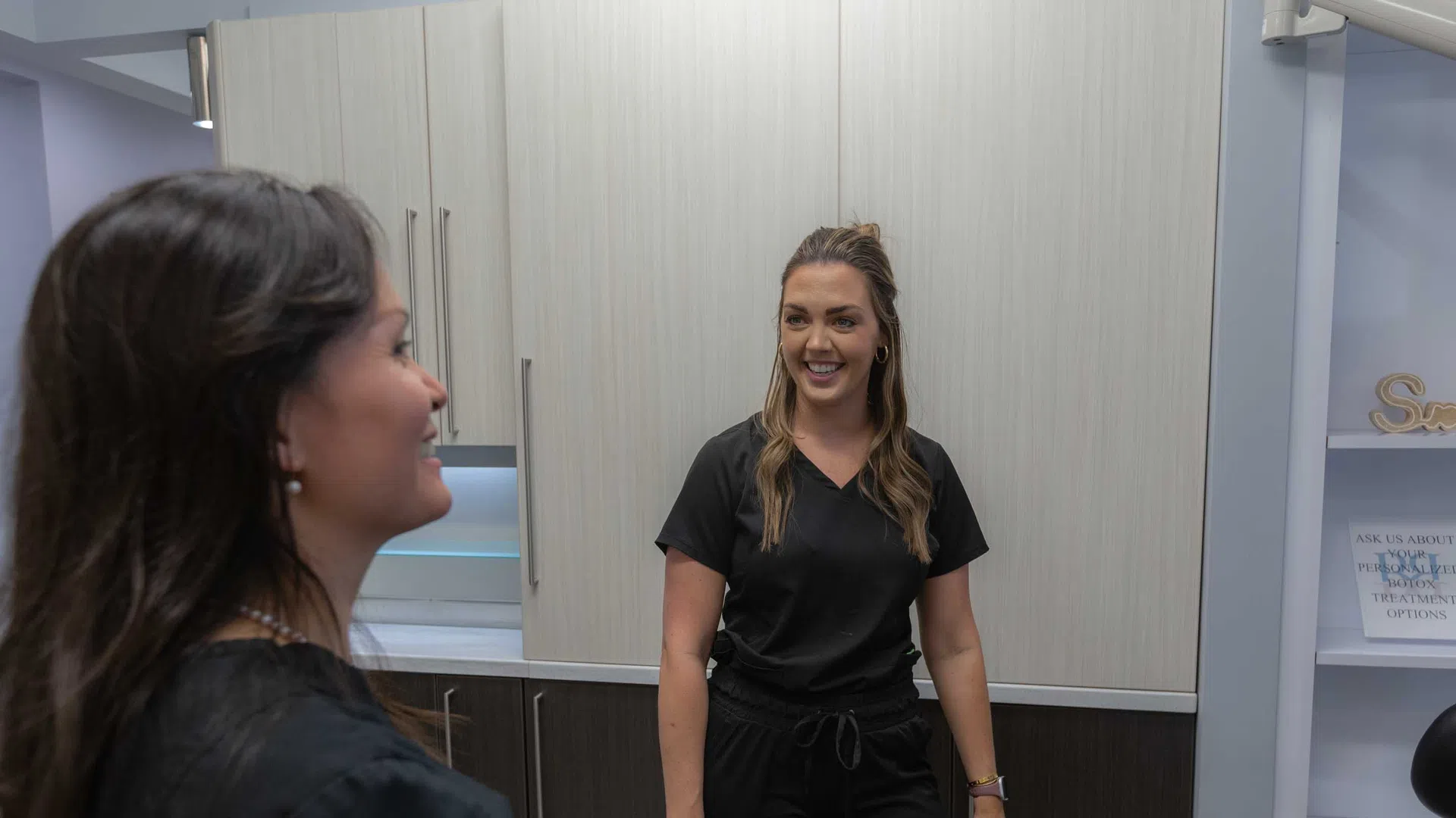 Dentist and female patient smiling and talking in a modern dental office setting.