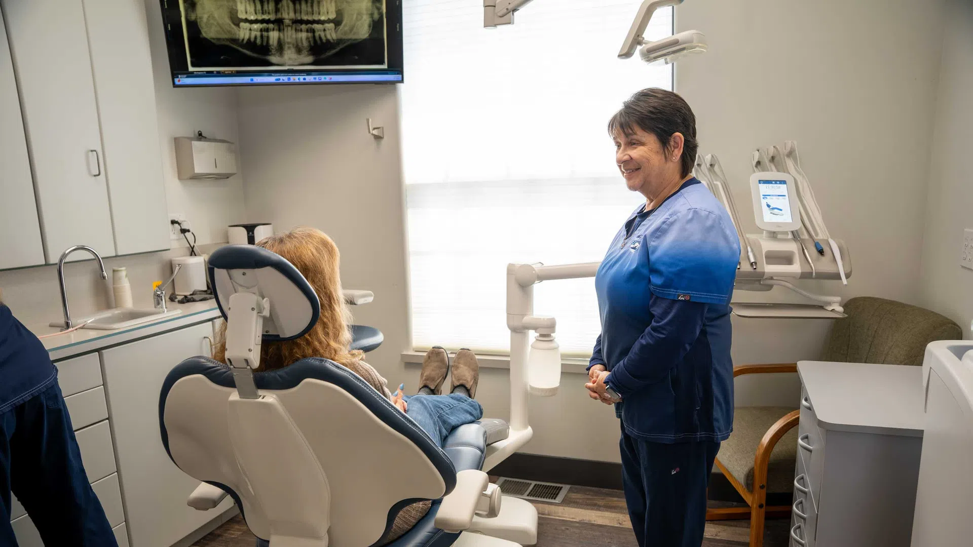 Dentist and patient in a modern dental office with dental chair, equipment, and a tooth x-ray on screen.