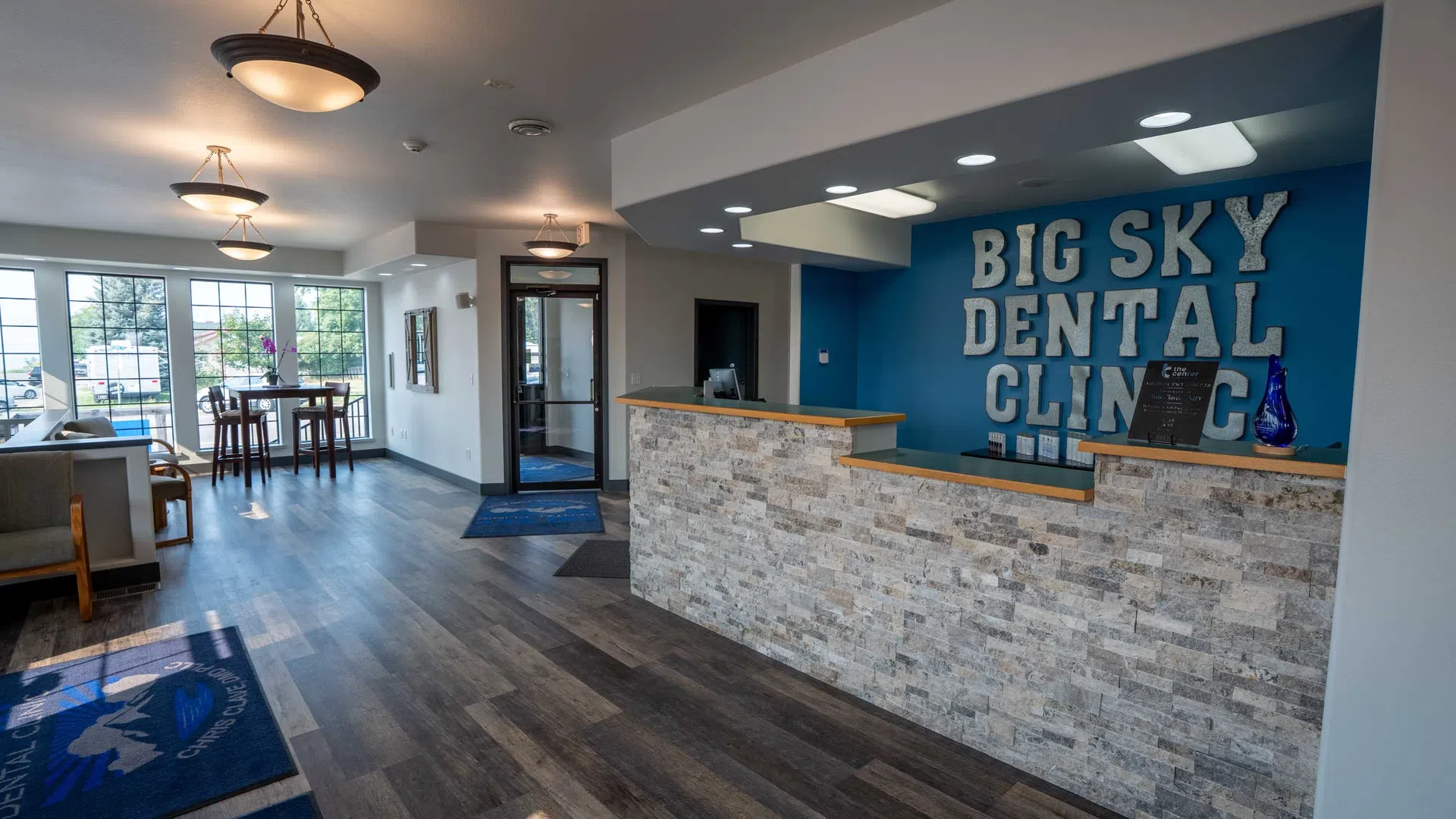 Modern dental clinic reception with stone desk, blue accent wall, and seating area near windows with natural light.