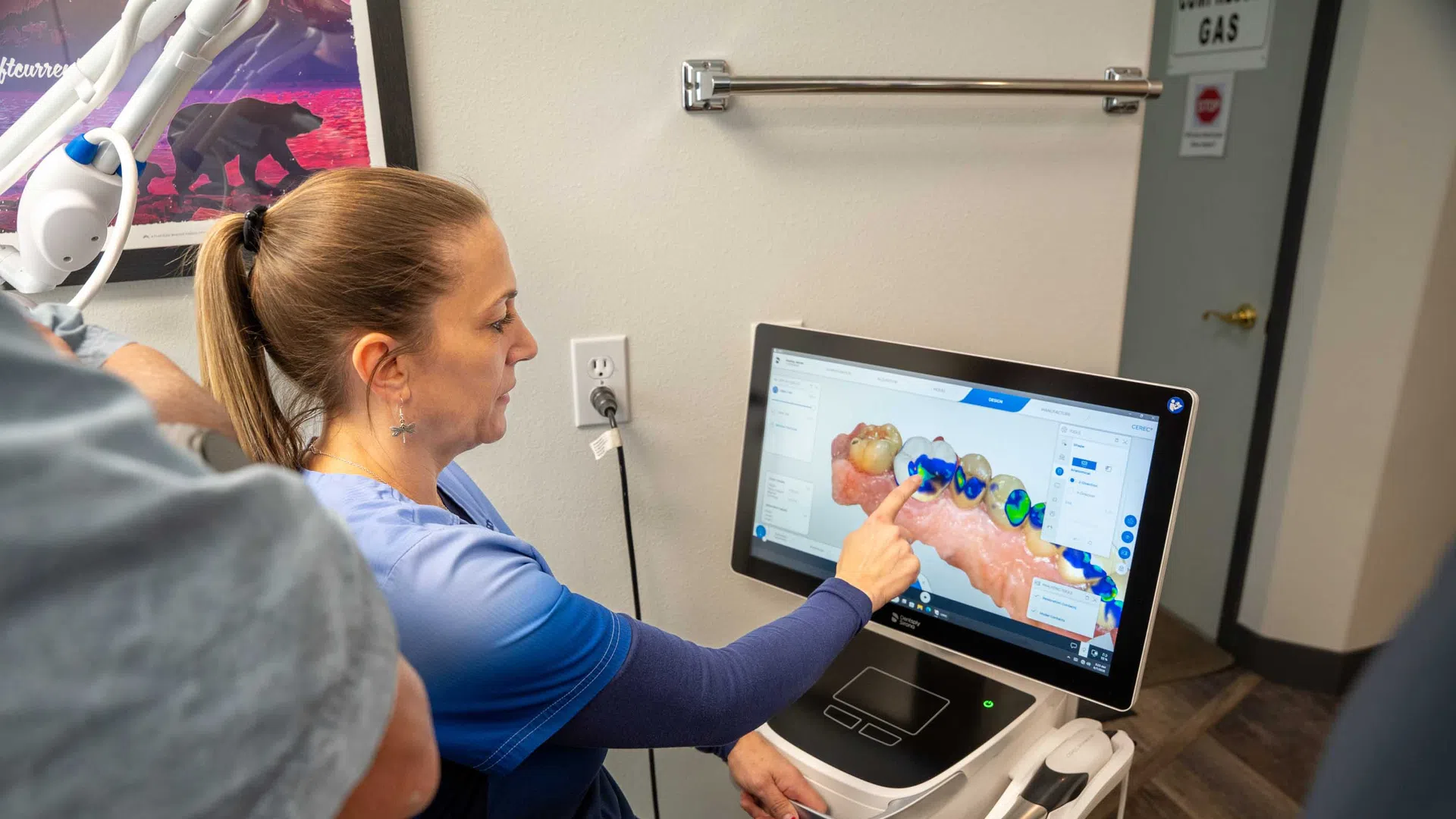 Dental professional demonstrating 3D tooth scan analysis on a touchscreen monitor in a clinic.