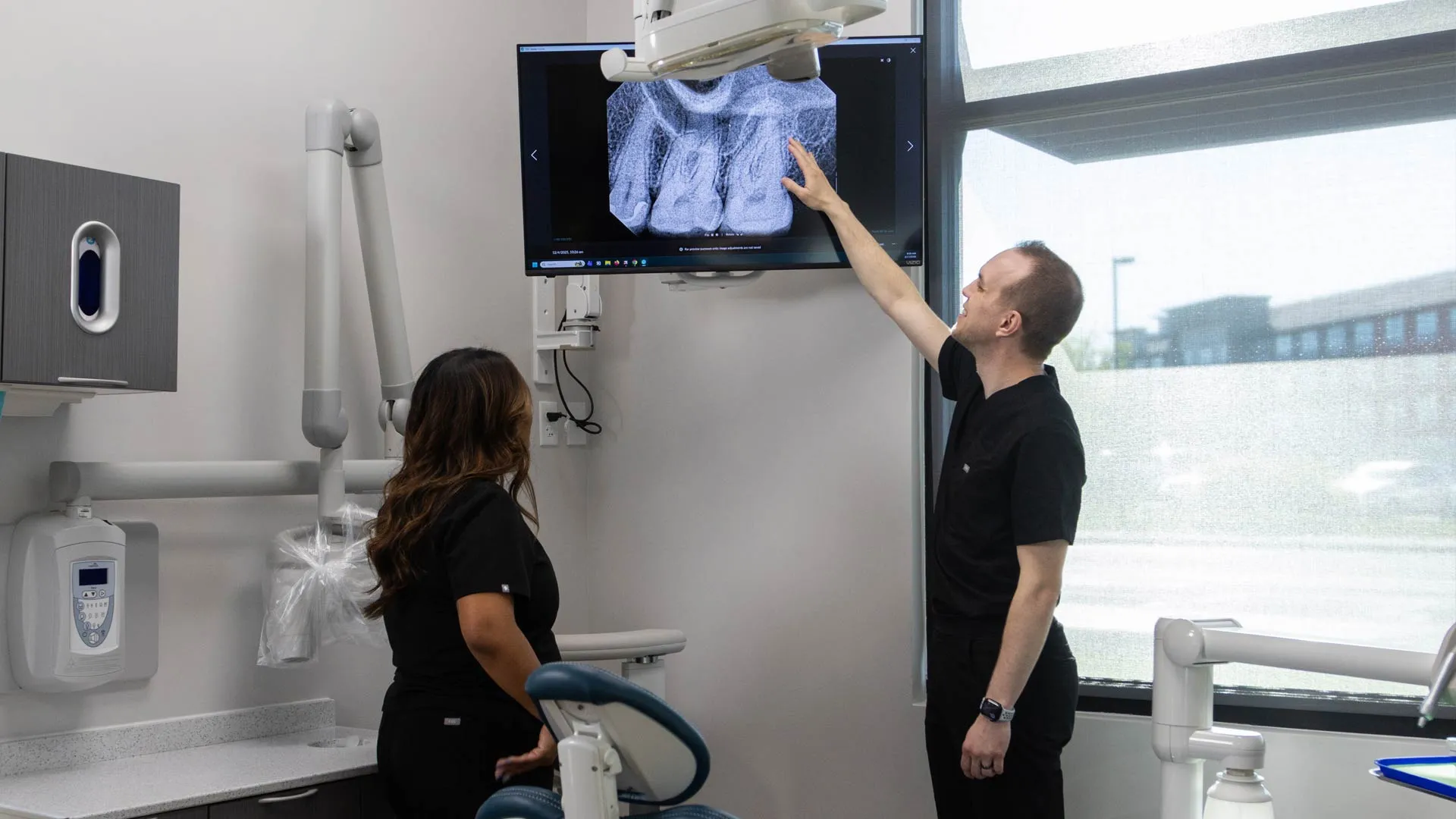 Dentists examining a digital dental X-ray on a screen inside a modern dental clinic room.
