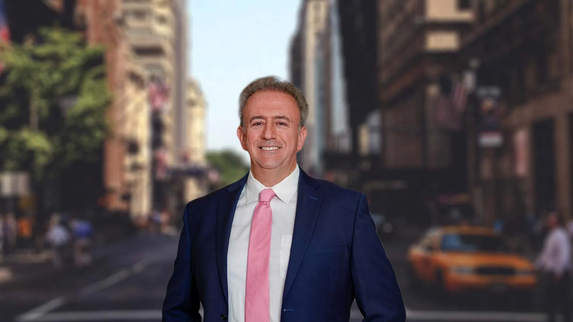 Smiling middle-aged man wearing black scrubs standing on a city street with blurred buildings and traffic in background