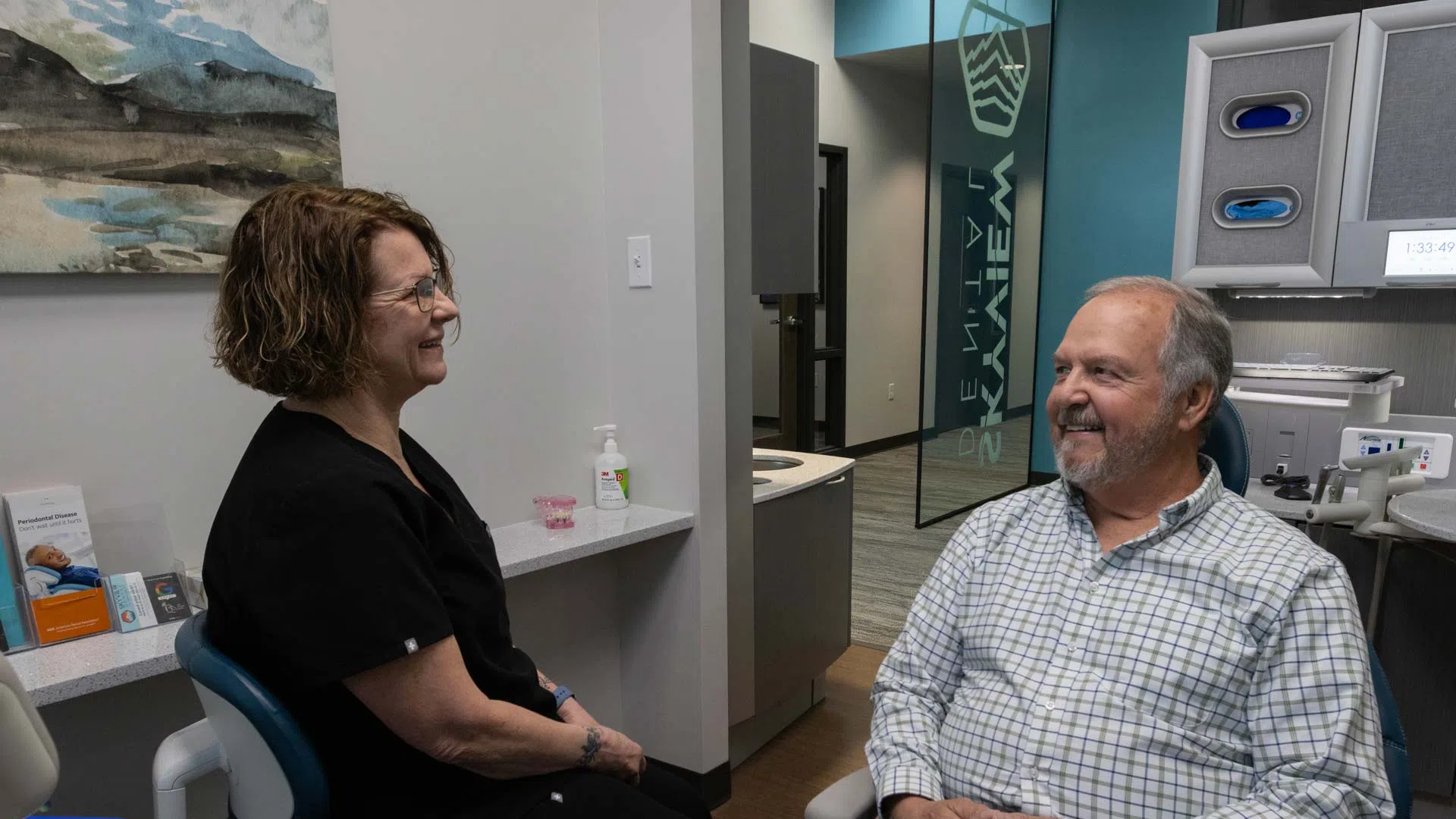 Dentist and senior male patient smiling while seated in a modern dental office consultation room.