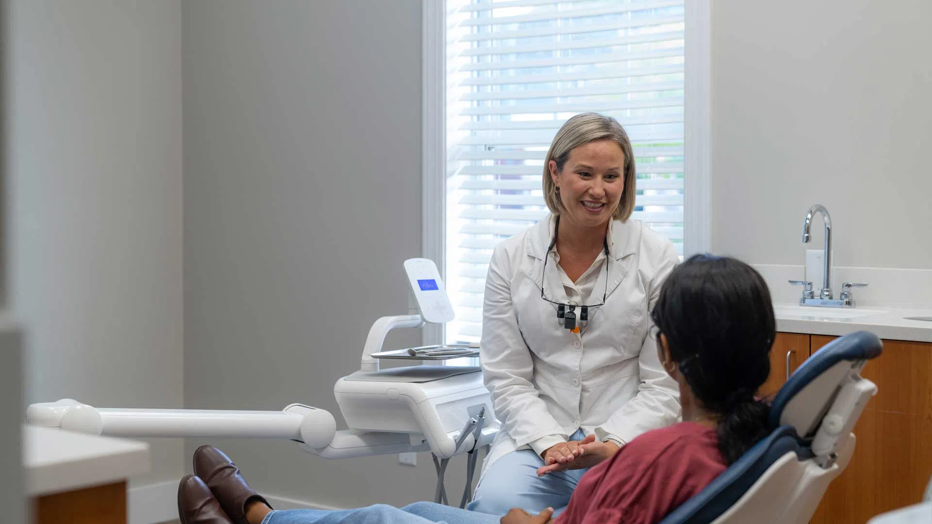 Female dentist smiling and talking to patient seated in dental chair during consultation.
