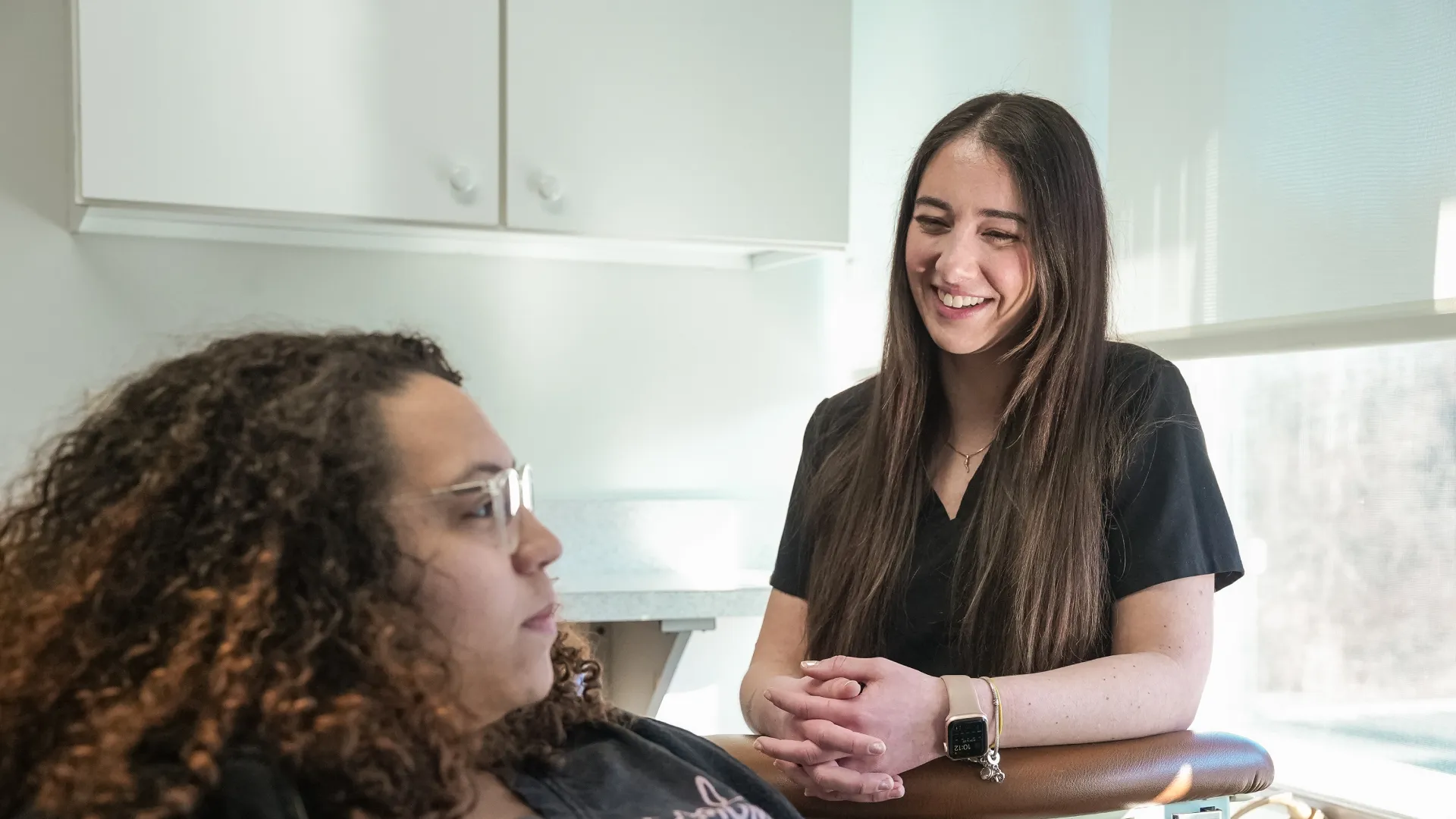 Smiling female healthcare professional listens attentively to patient in a bright medical office setting.