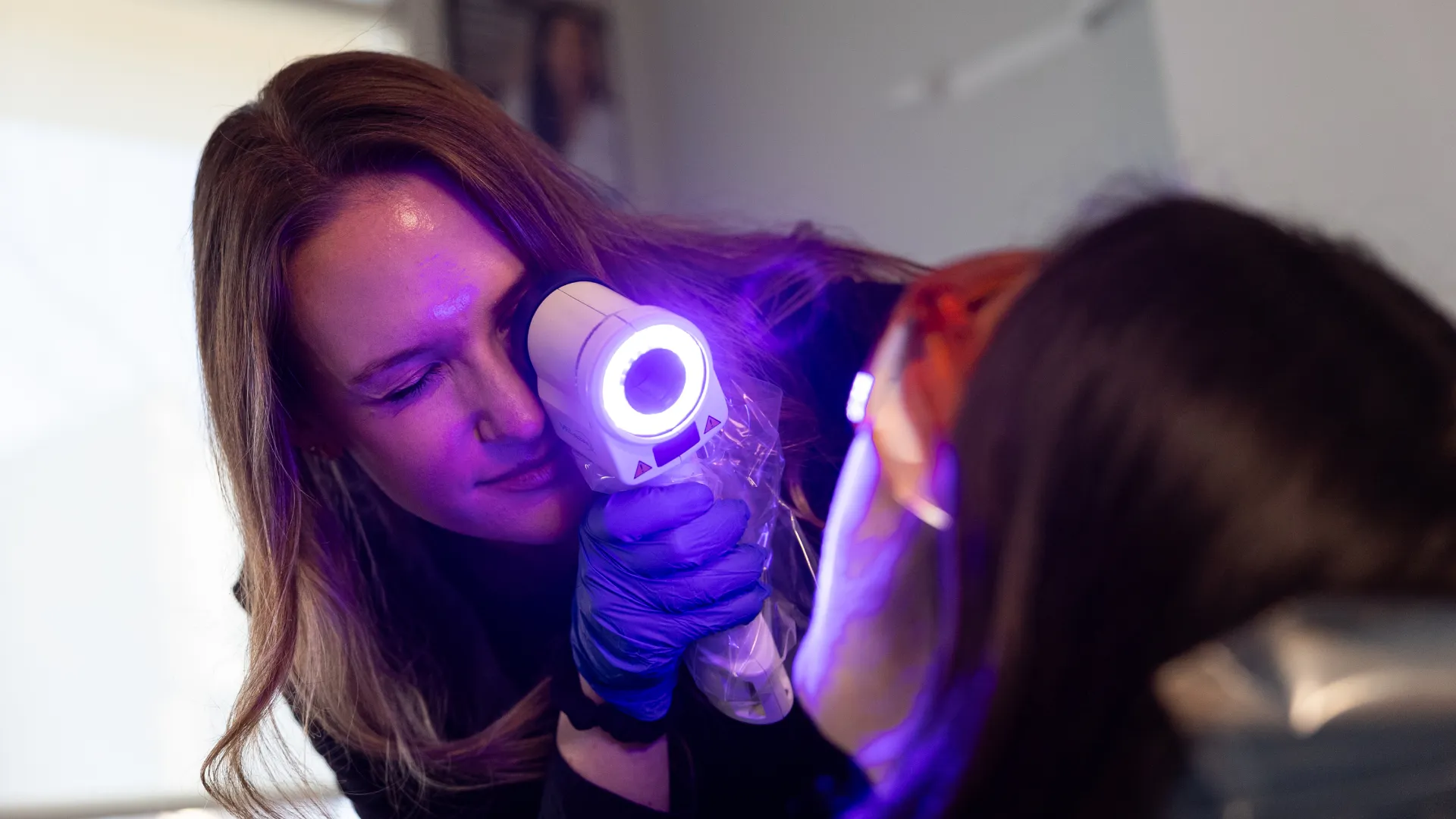 Dermatologist using a handheld UV light device to examine patient's skin in a clinical setting.