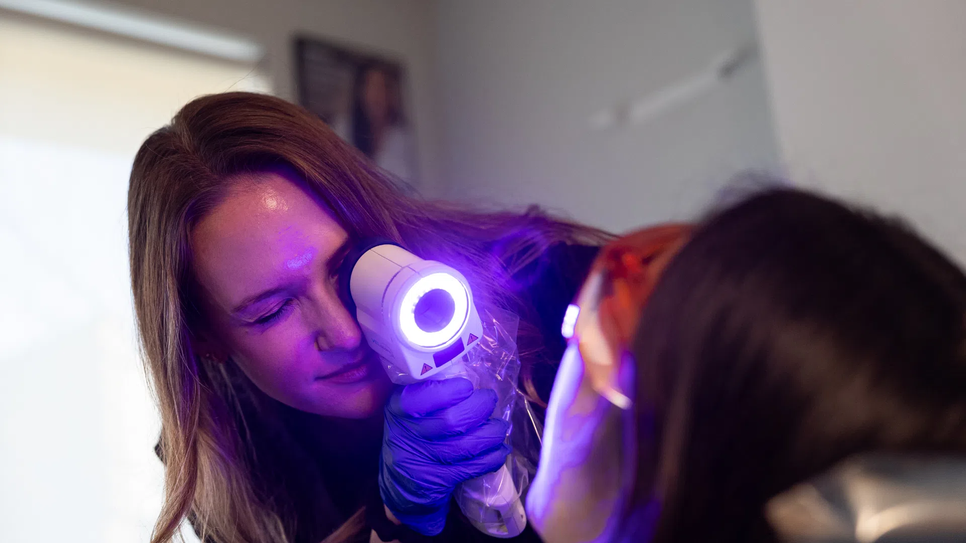 Dermatologist using a handheld UV light device to examine patient's skin in a clinical setting.