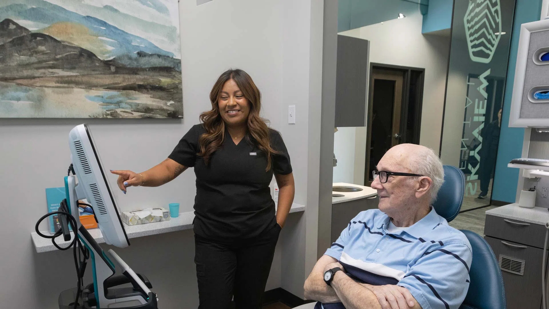Dental professional reviews information on screen with elderly male patient in modern clinic room.