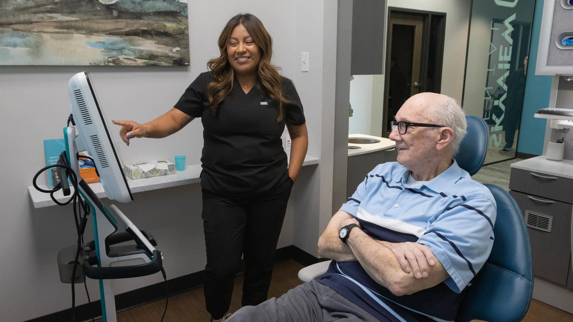 Healthcare professional explaining information on monitor to elderly patient in a medical office setting.