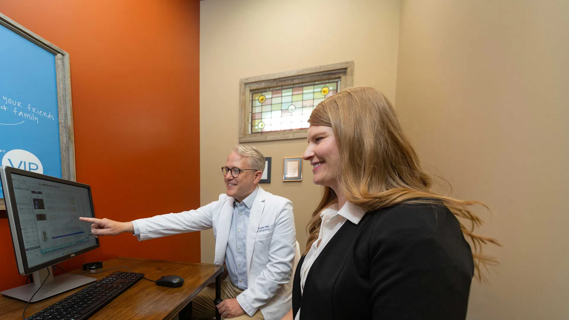 Doctor explaining medical results on a computer screen to a smiling female patient in an office setting.