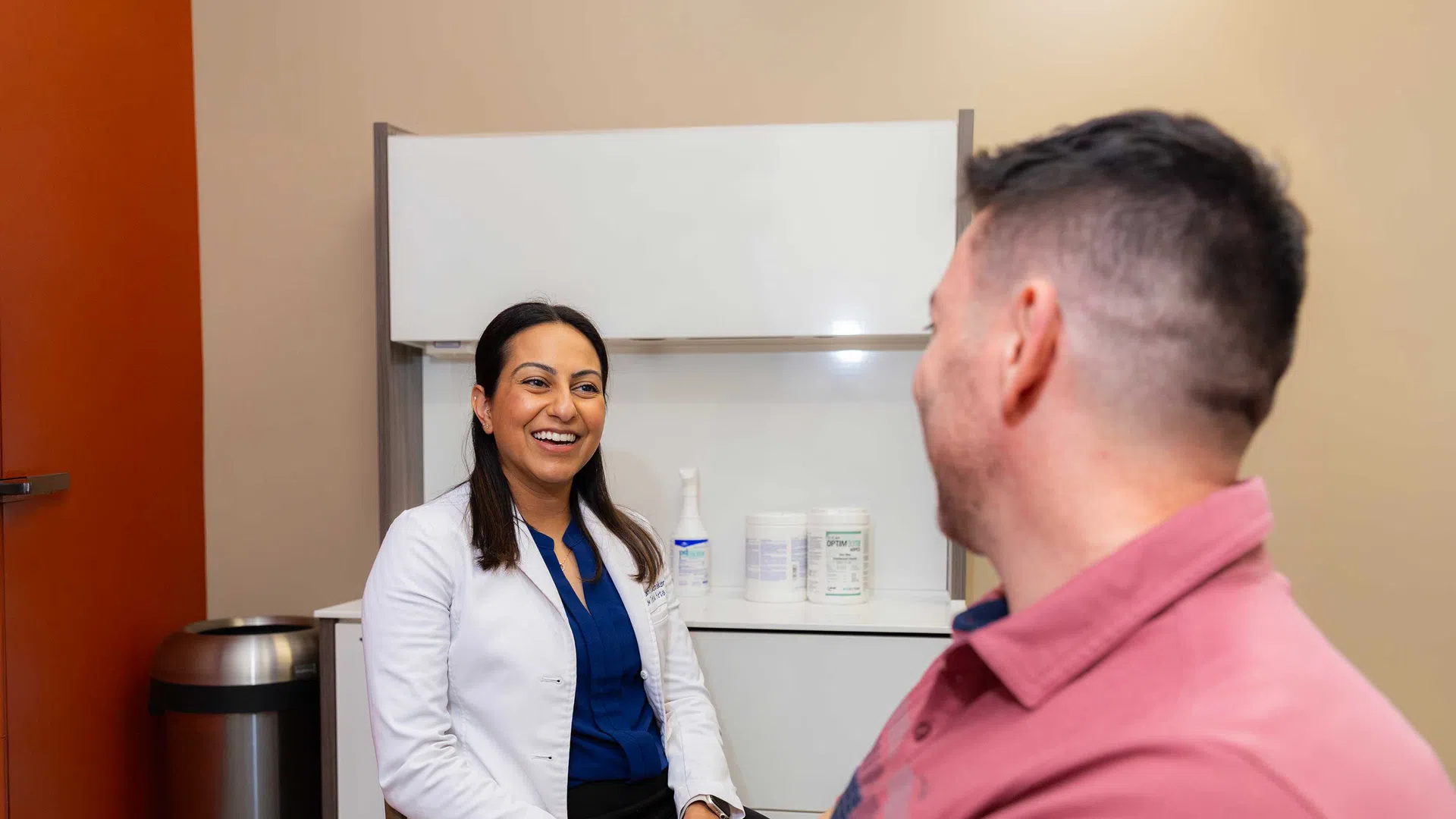 Female doctor smiling and talking to a male patient during a consultation in a medical office.