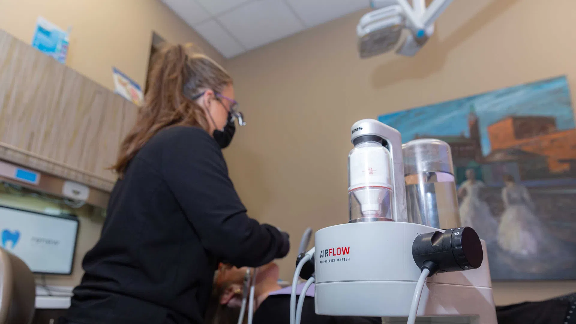 Dental hygienist uses airflow machine for patient teeth cleaning in a modern clinic setting.