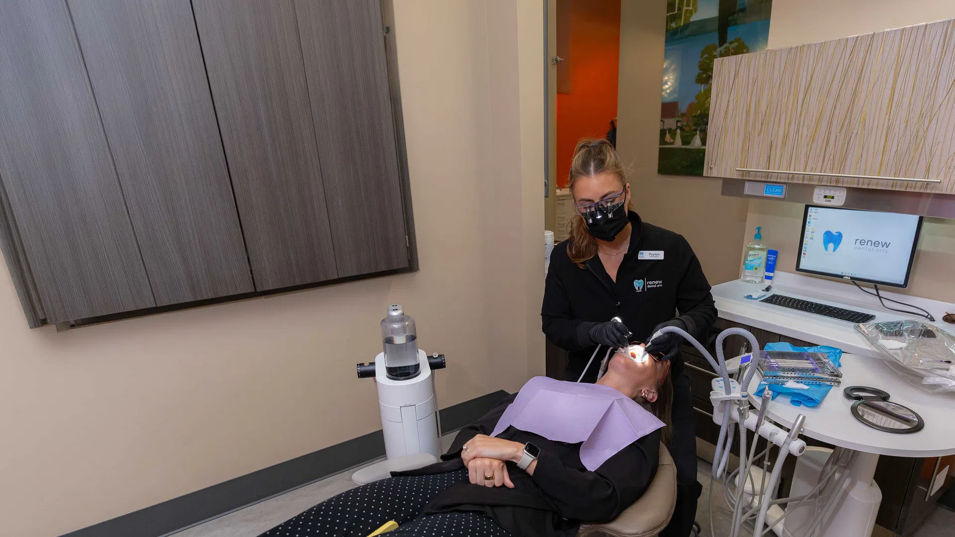 Dentist wearing black mask treating patient reclining in dental chair in modern clinic