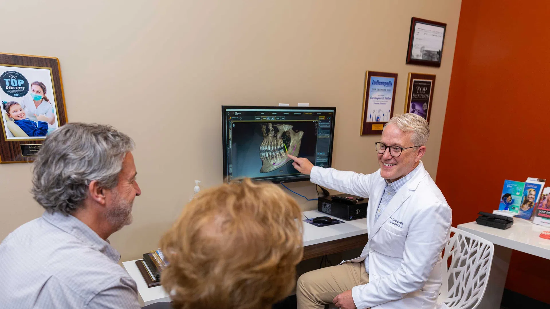 Dentist explaining dental X-ray results to a middle-aged couple in a modern consultation room.