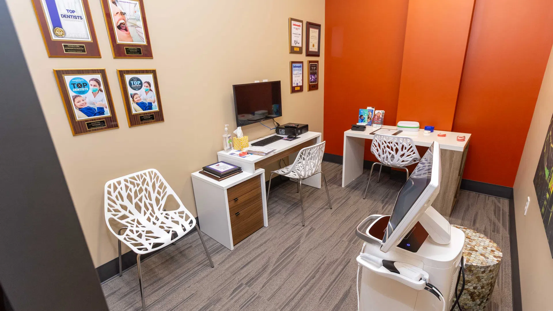 Modern dental office consultation room with contemporary chairs, computer station, and award plaques on wall.