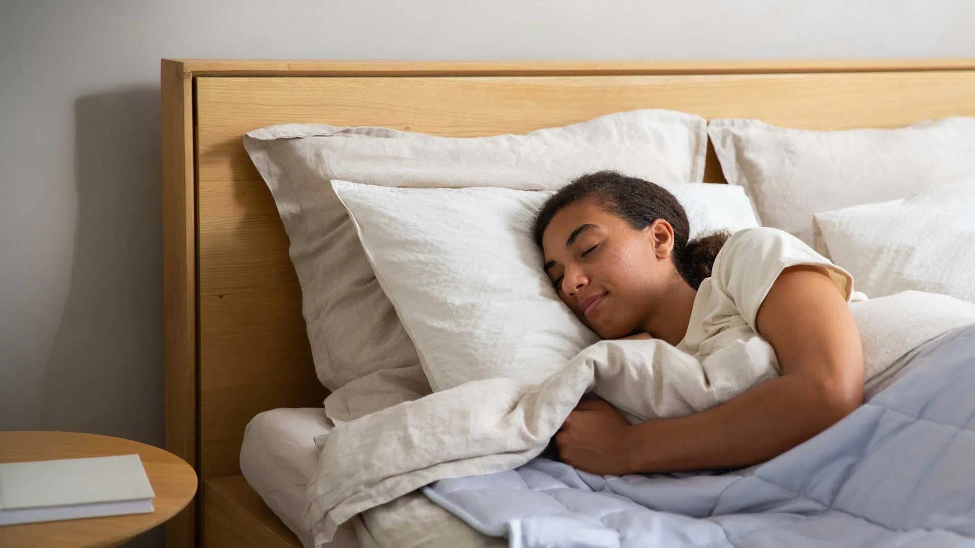 Woman peacefully sleeping on a bed with white pillows and beige bedding in a cozy bedroom.