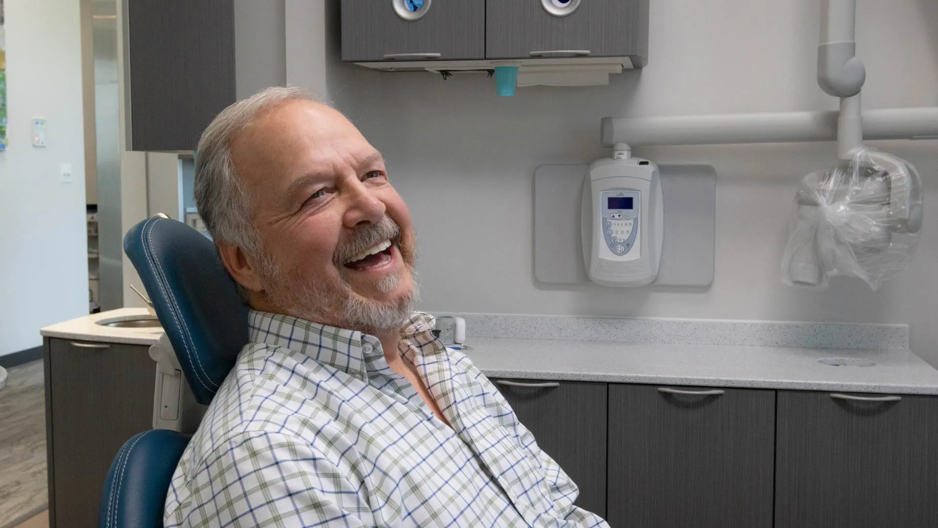 Smiling elderly man sitting in a dental chair in a modern dental office with white and gray decor.